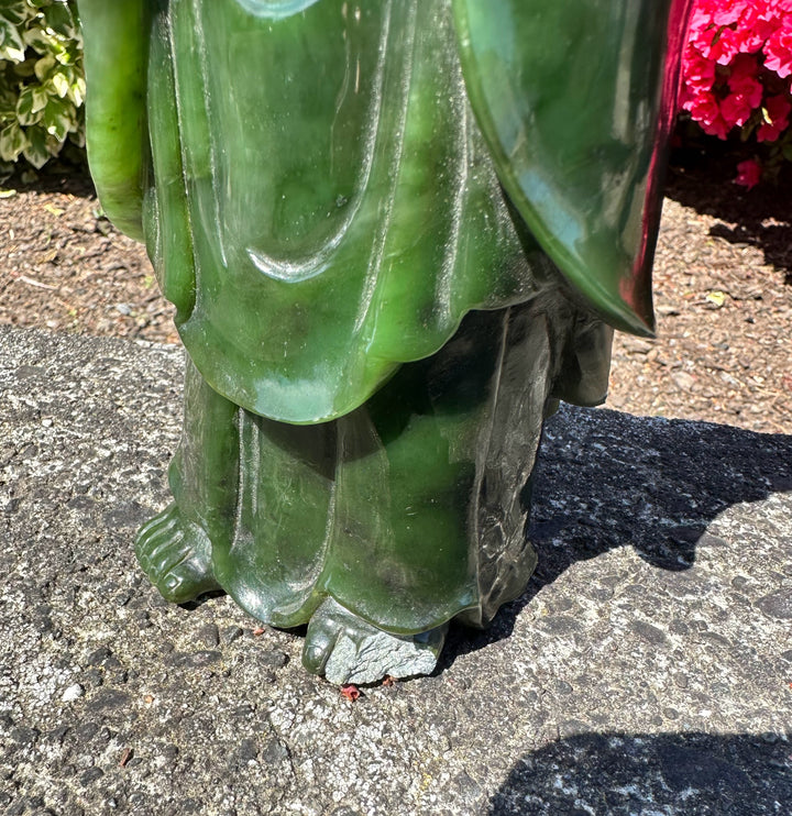 Close-up of the jade Guanyin statue base showing flowing robes and feet on a rough concrete surface