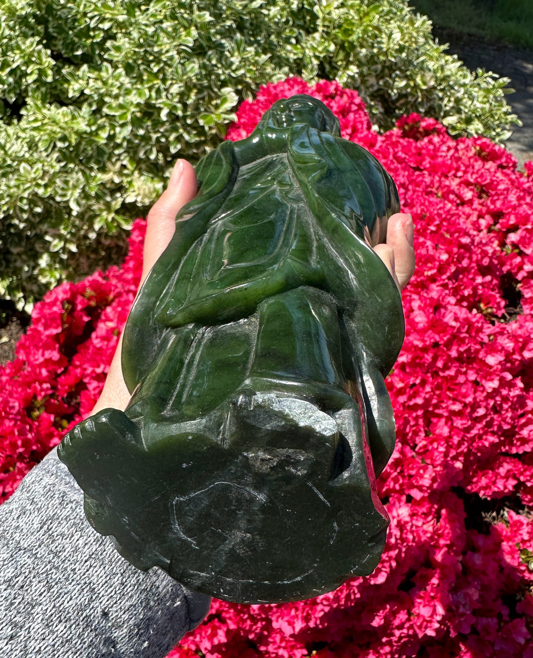 Close up of a dark green Jade Guanyin statue being held outdoors showing back and flowing robes