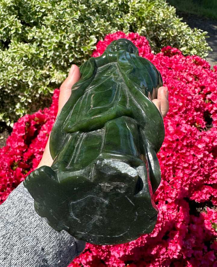 Close up of a dark green Jade Guanyin statue being held outdoors showing back and flowing robes