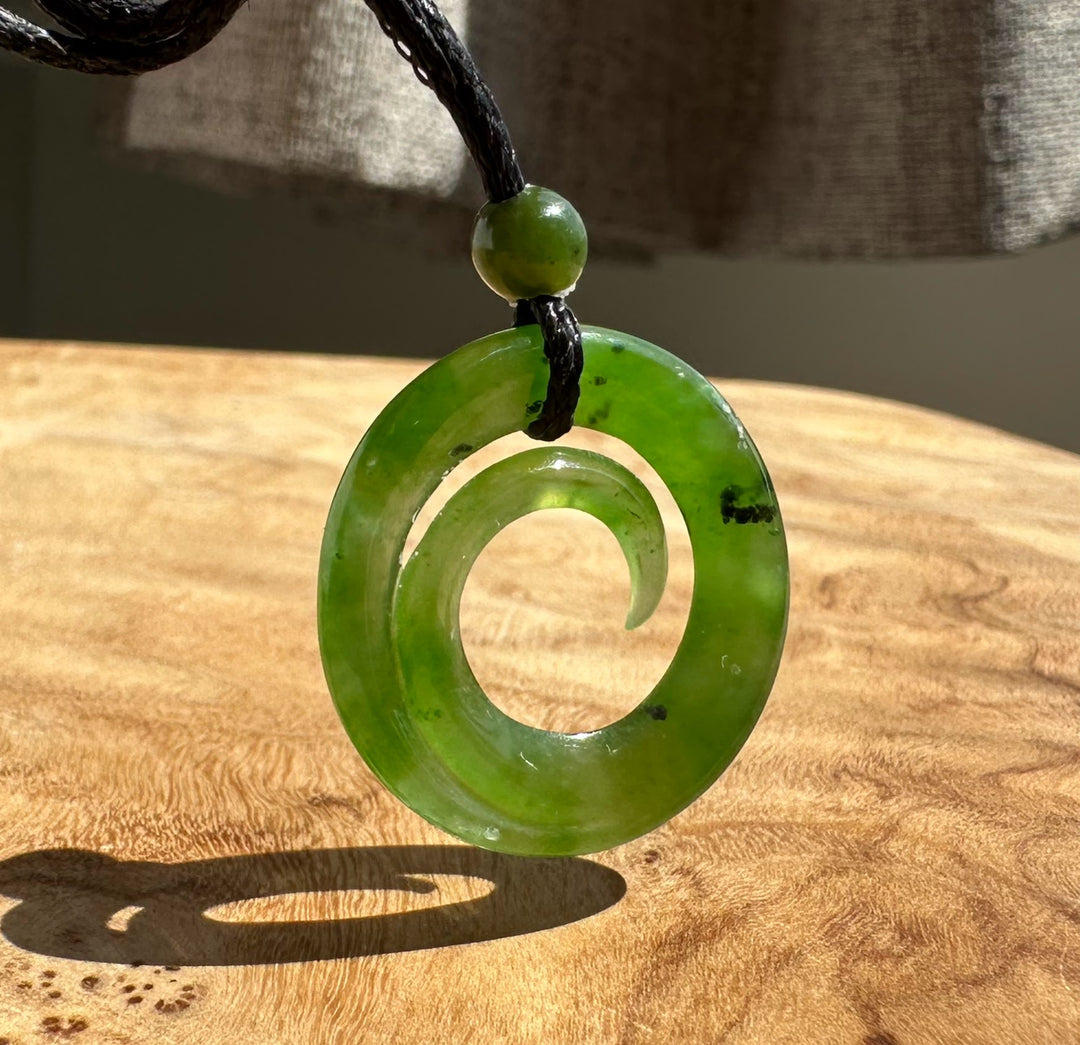 A green stone spiral pendant necklace with a black cord, resting on a wooden surface.