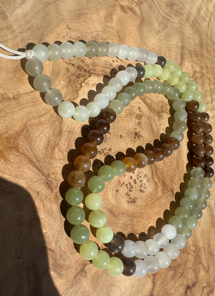 Jade 6mm round beads in shades of green, brown, gray, and white, arranged on a textured wooden surface.