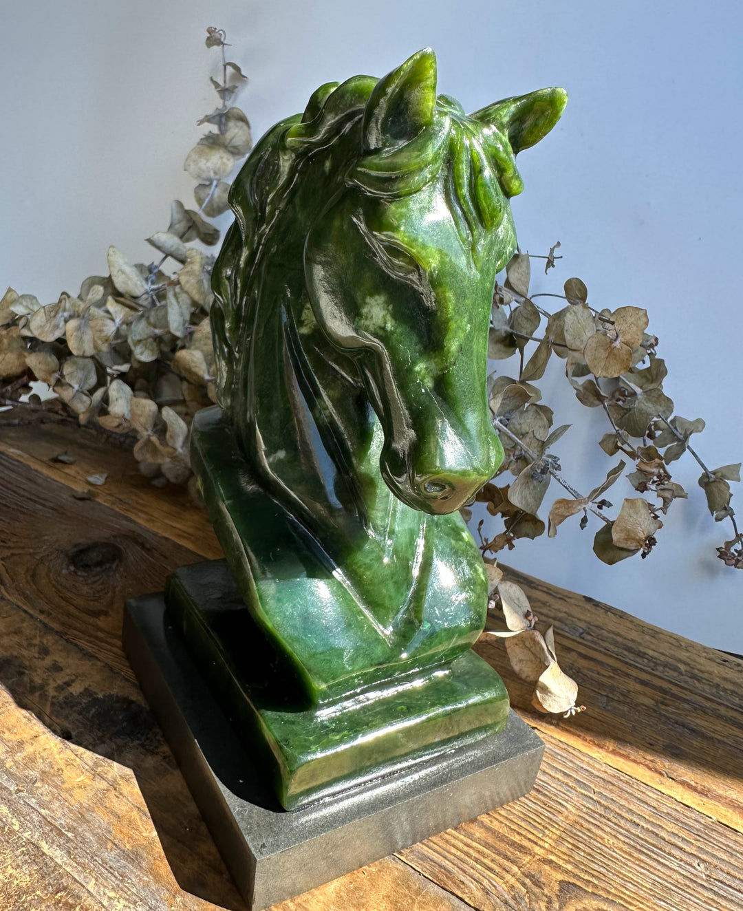 Side view of a glossy green nephrite jade horse bust with a flowing mane on a rectangular pedestal.