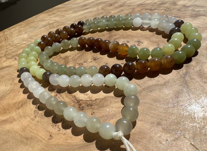 A set of nephrite beads made from natural jade, featuring shades of green, brown, white, and gray, arranged on a wooden surface.