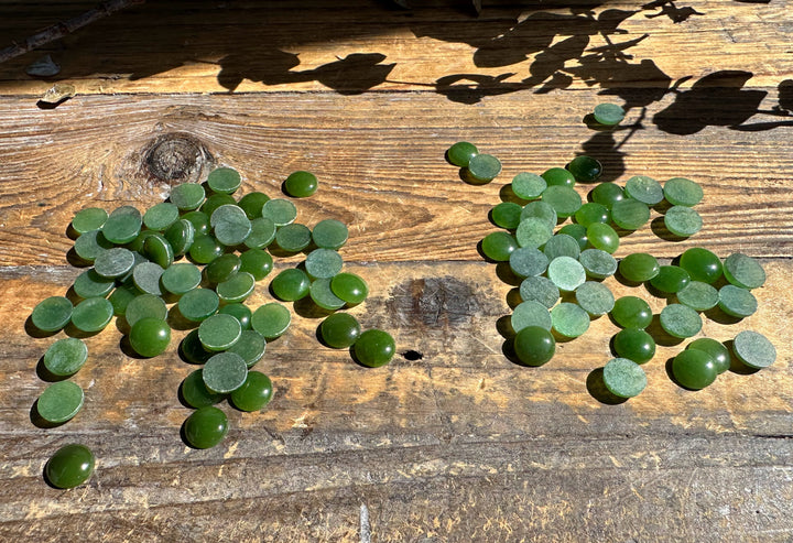 Green 9mm round cabochons scattered across a rustic wooden surface
