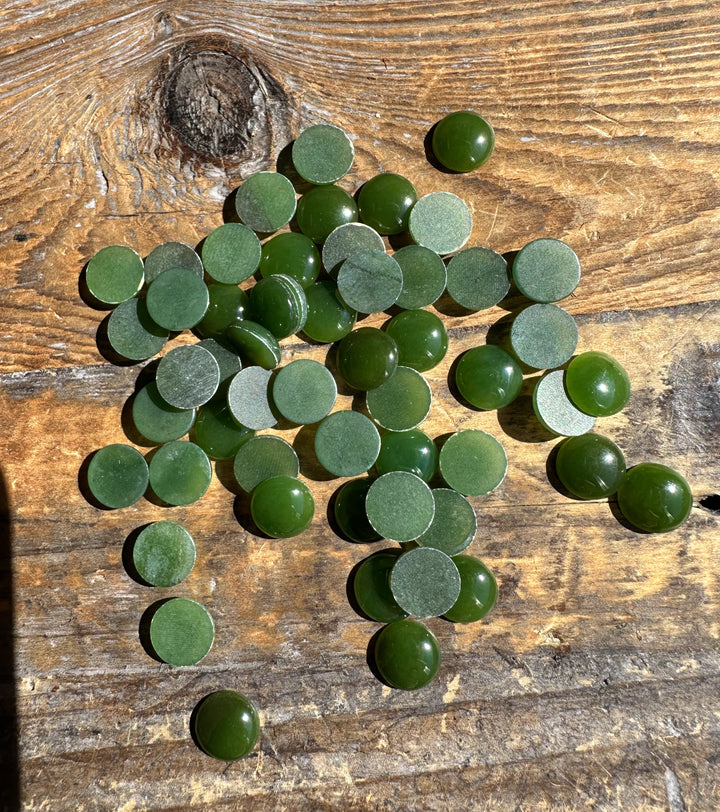 Green 9mm round cabochons scattered on a weathered wooden surface