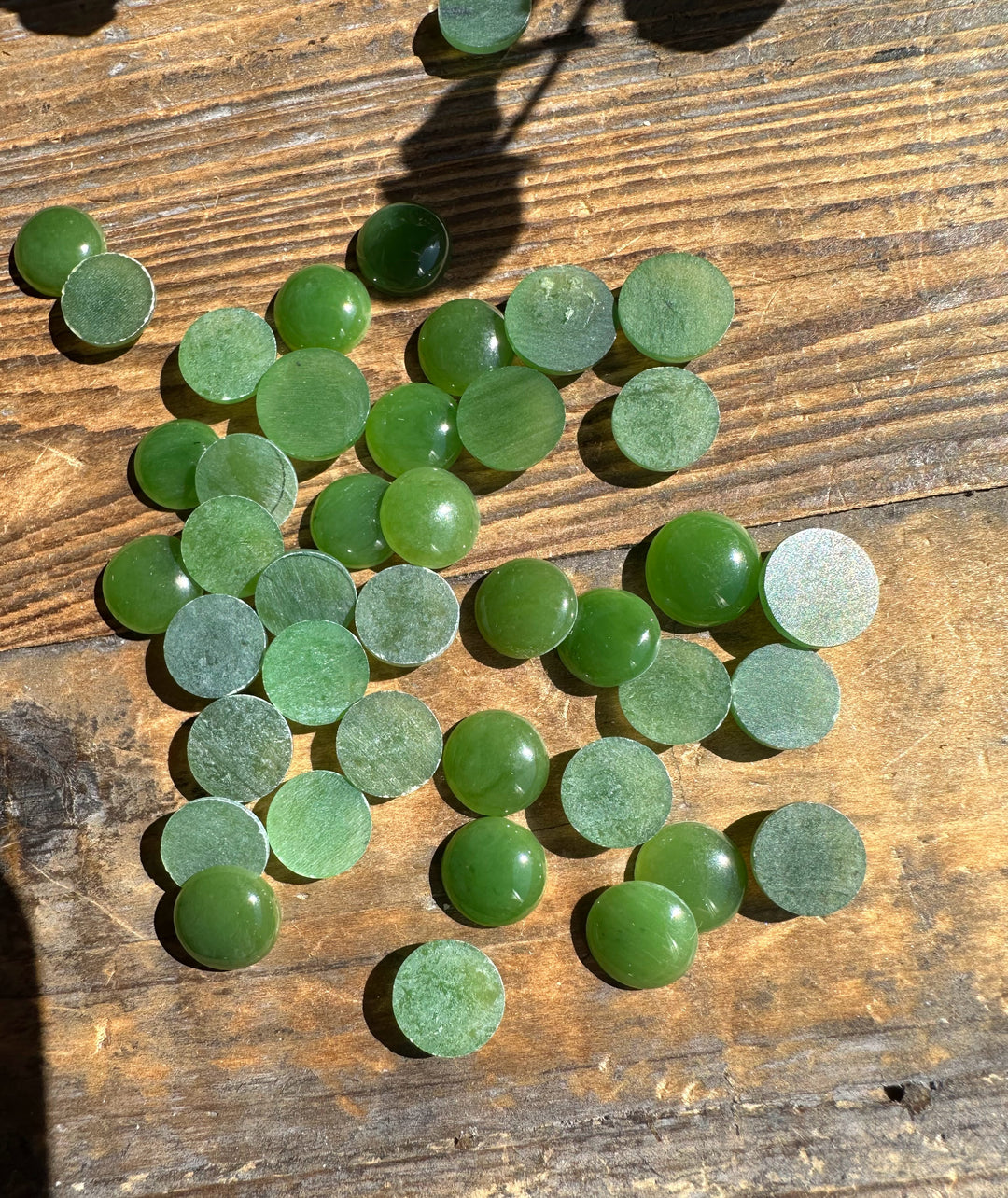 Green 9mm round cabochons with flat backs spread across a wooden surface