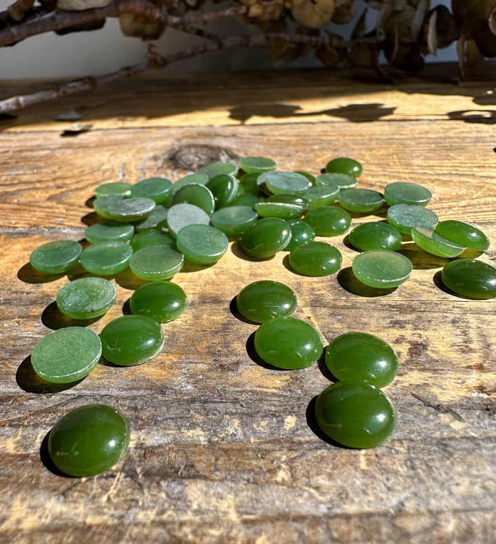 Assorted green 9mm round cabochons spread on sunlit wooden plank