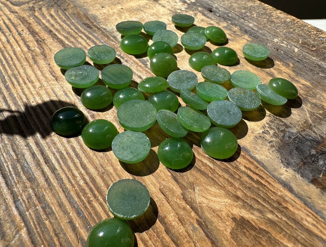 Green 9mm round cabochons on sunlit wood with some backs visible