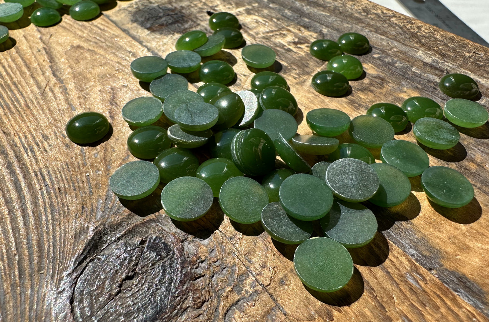 Close up of flat-backed green 9mm round cabochons on weathered wood