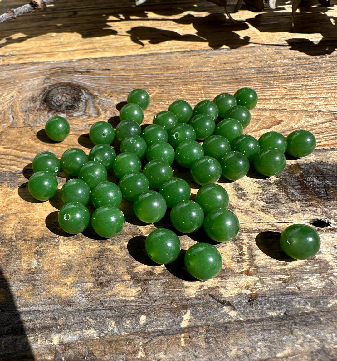 A+ half drilled 8mm Canadian jade beads scattered on a weathered wooden surface