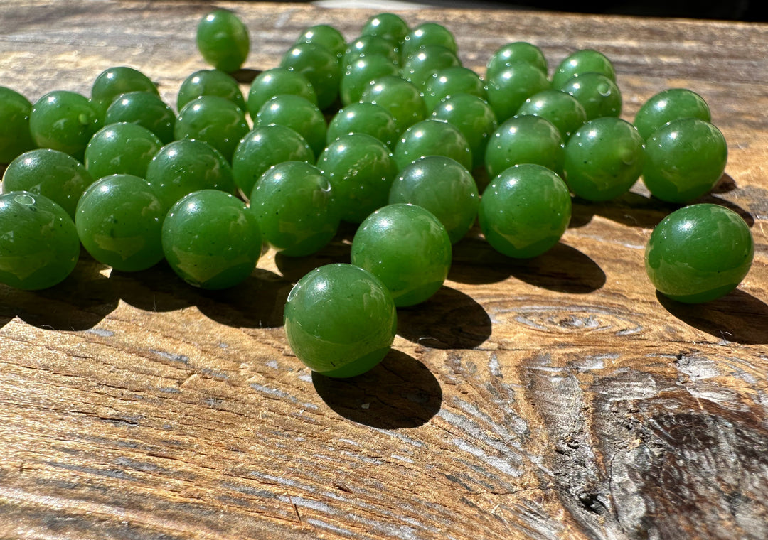 Group of 8mm Canadian jade beads on a sunlit wooden surface with half drilled holes