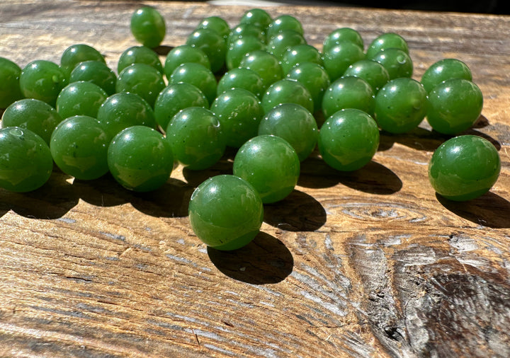 Group of 8mm Canadian jade beads on a sunlit wooden surface with half drilled holes