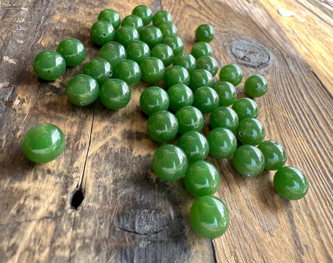 Close up of multiple green jade beads on wood showing round shapes and drill holes for stringing
