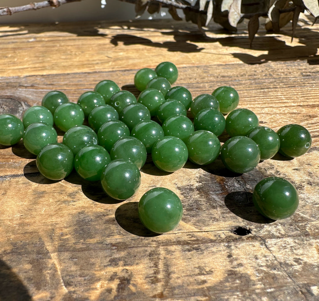 A+ Half Drilled 10mm Canadian Jade beads clustered on a sunlit wooden surface
