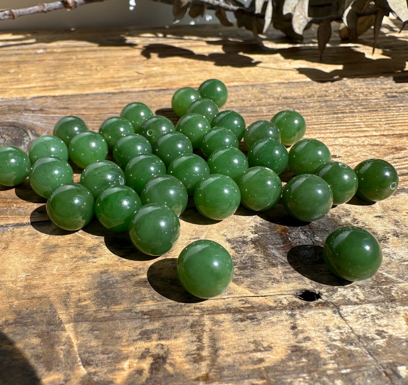 A+ Half Drilled 10mm Canadian Jade beads clustered on a sunlit wooden surface
