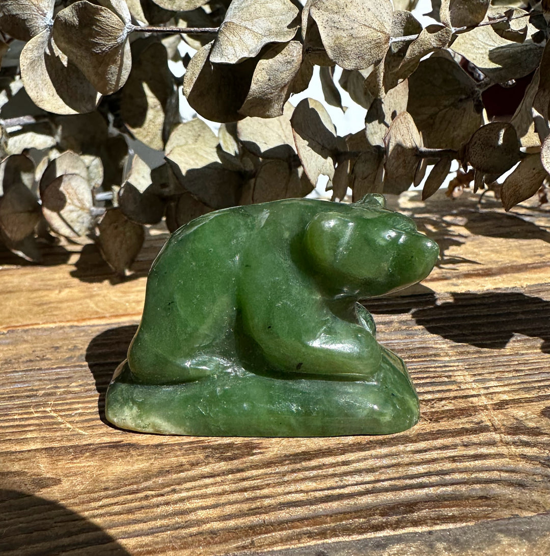 Small jade bear figurine on a wooden surface with dried beige leaves in the background