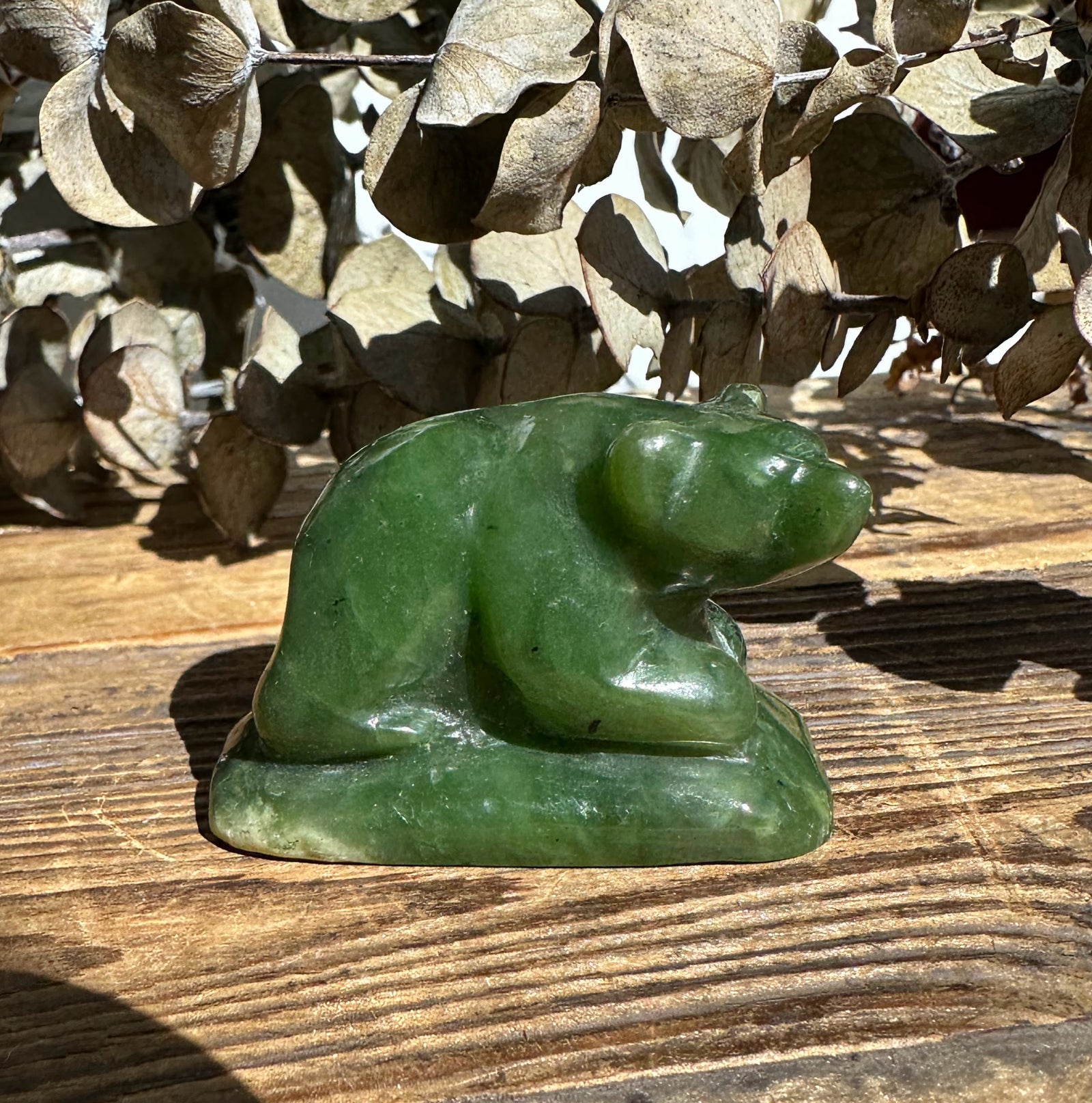 Small jade bear figurine on a wooden surface with dried beige leaves in the background