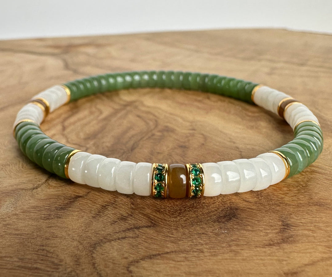 A beaded stretch bracelet featuring textured green and smooth white beads, accented with gold spacer rings and central green crystal-encrusted brown beads, displayed on a wooden surface.