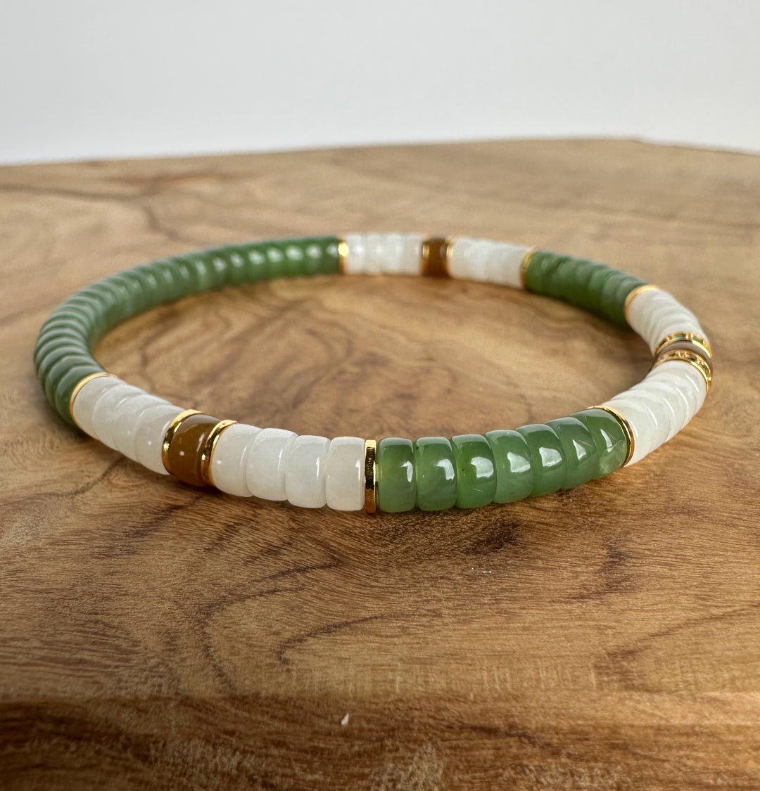A beaded stretch bracelet featuring alternating green and white cylindrical beads, accented with small gold spacer rings, displayed on a wooden surface.