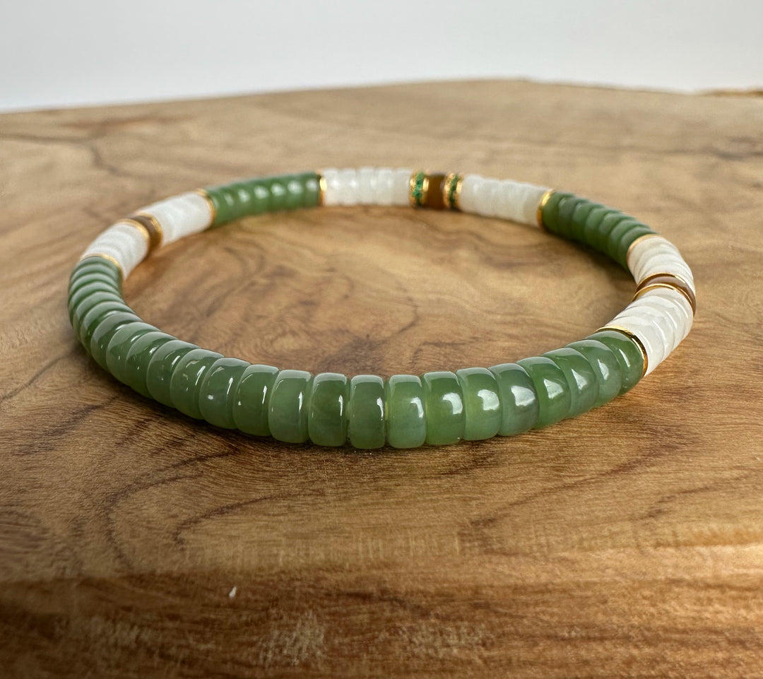 A beaded stretch bracelet featuring textured green and smooth white beads, accented with small gold spacer rings, displayed on a rustic wooden surface.