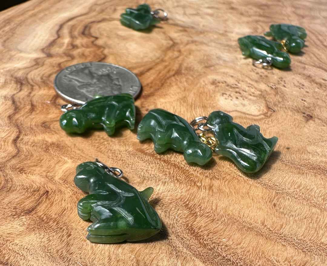 Five green carved monkey charms with small gold-colored metal loops, displayed on a textured wooden surface next to a US quarter for scale.