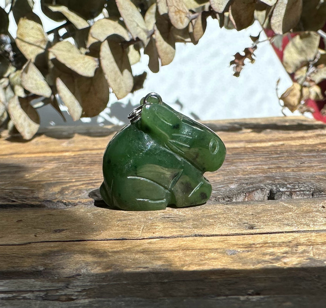 Green nephrite jade bunny pendant with a metal bail on top, set on a rustic wooden surface.