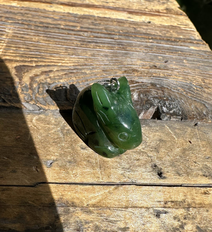 Green Canadian nephrite jade bunny pendant with a metal bail, photographed on weathered wood.