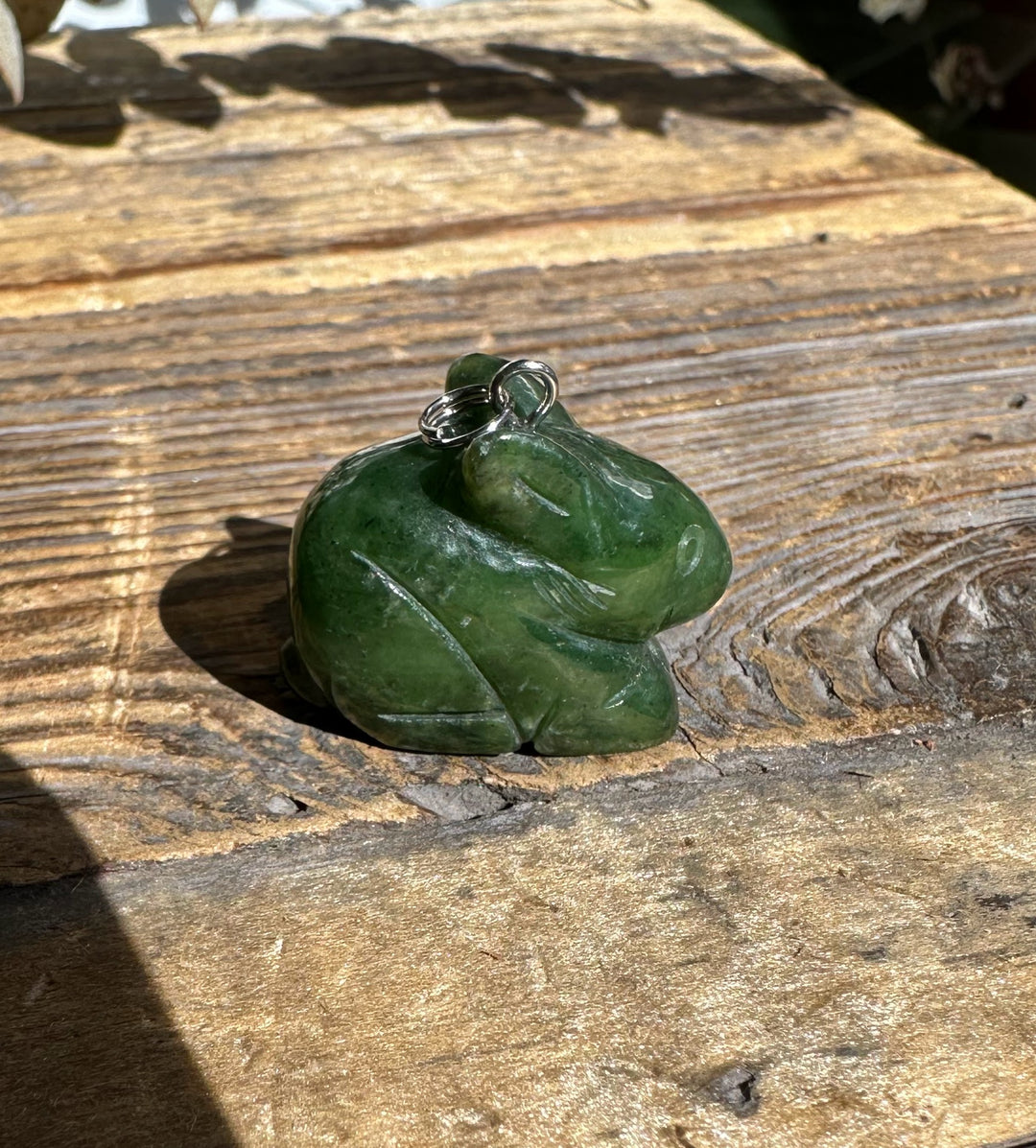 Green nephrite jade bunny pendant with a silver bail resting on weathered wood.