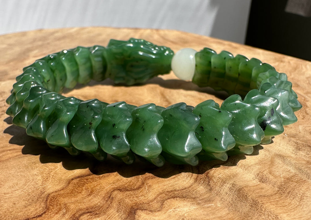 A carved green jade bracelet with a dragon head and scale pattern, displayed on a wooden surface.