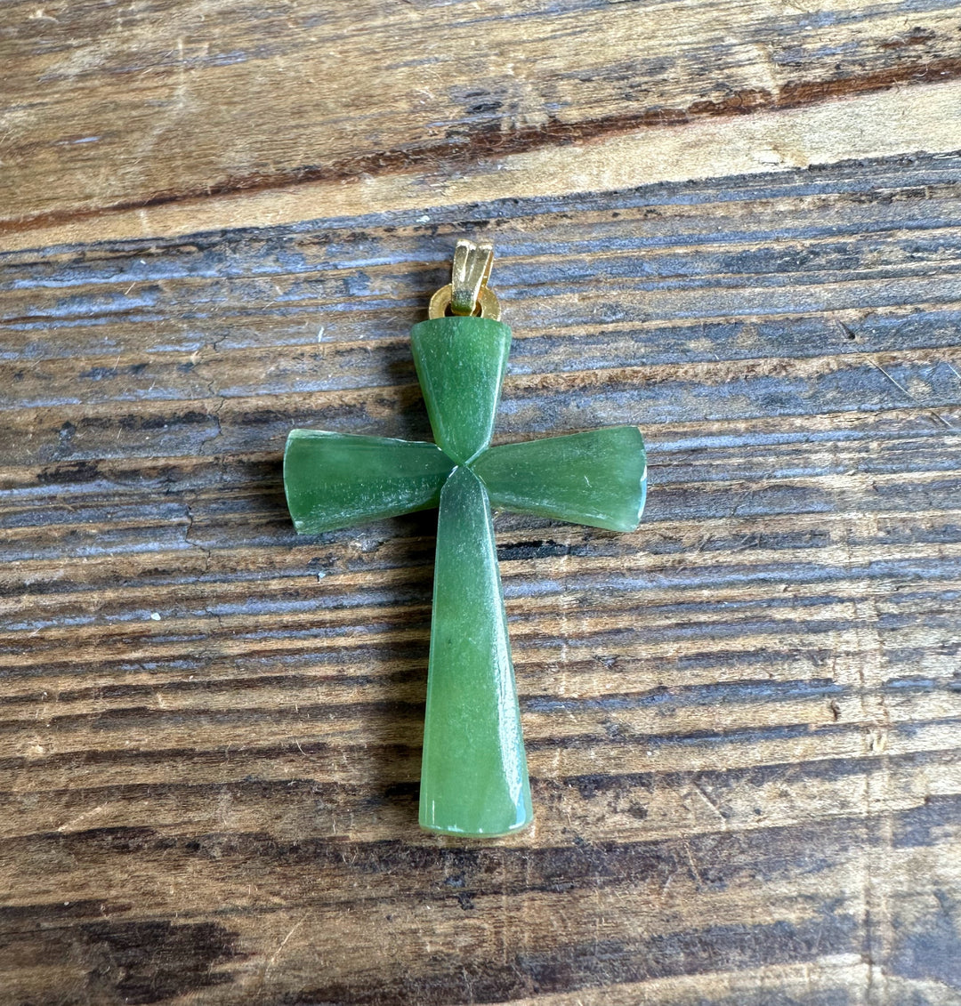 Green jade cross pendant with gold bail on wood surface