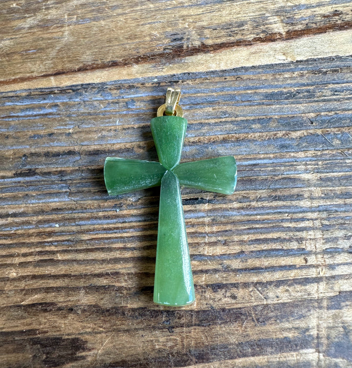 Green jade cross pendant with gold bail on wood surface