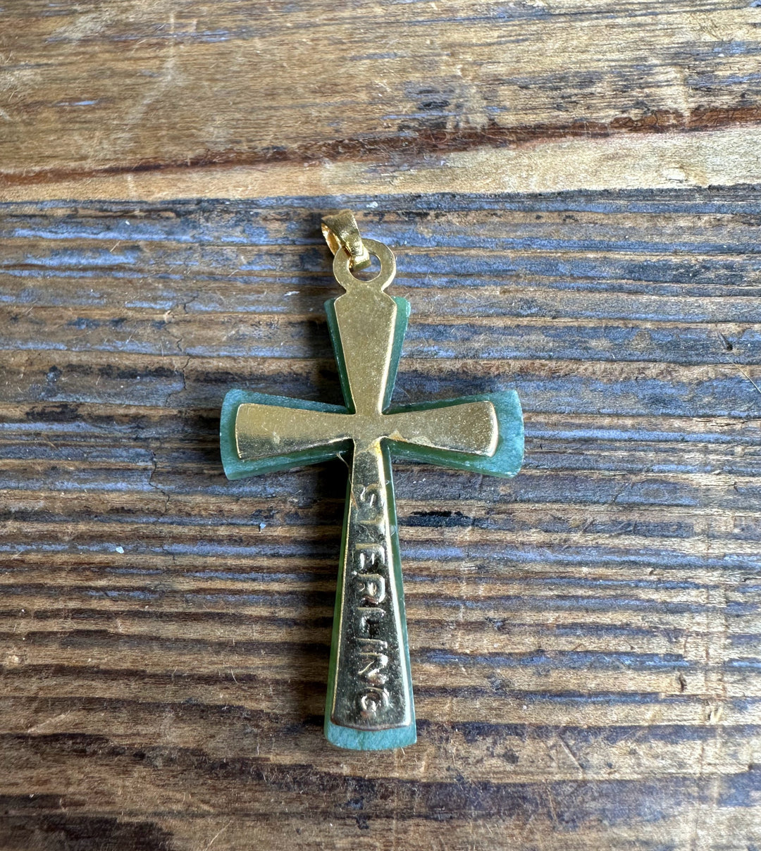 Vintage jade cross pendant with gold trim on wood background