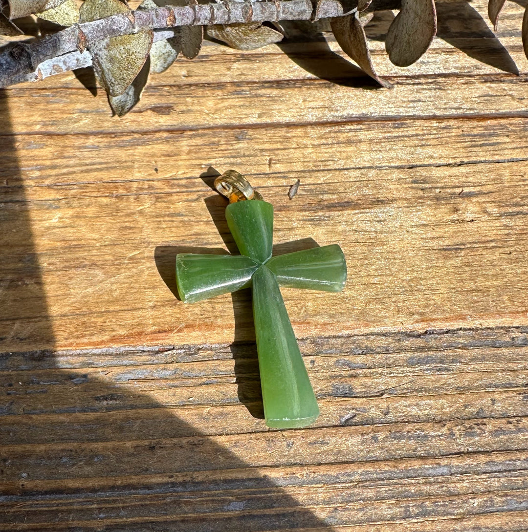 Long green jade cross pendant with a loop bail on a weathered wooden surface.
