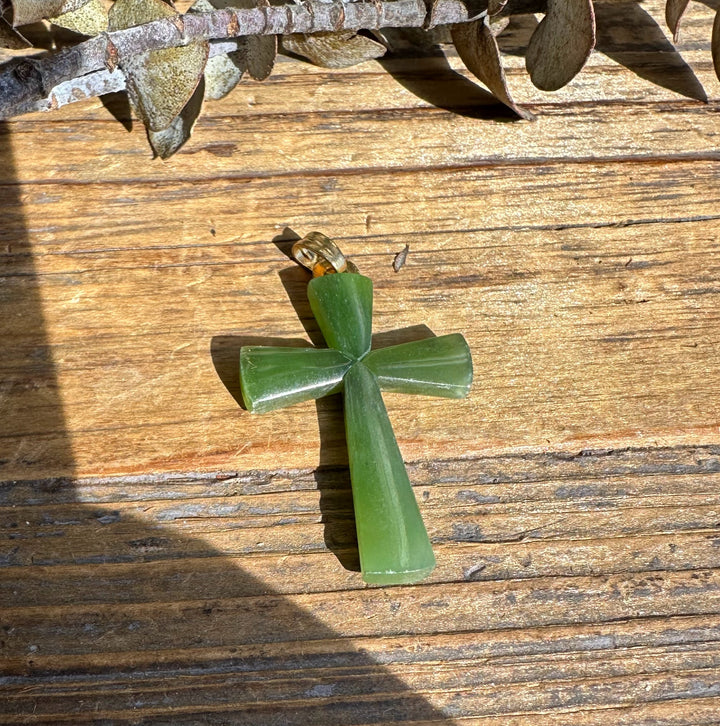 Long green jade cross pendant with a loop bail on a weathered wooden surface.