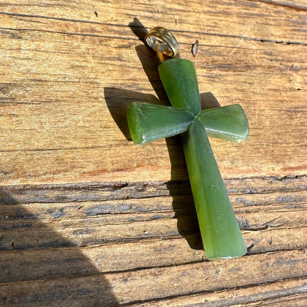 Vintage green jade cross pendant with a metal bail on a wooden surface.