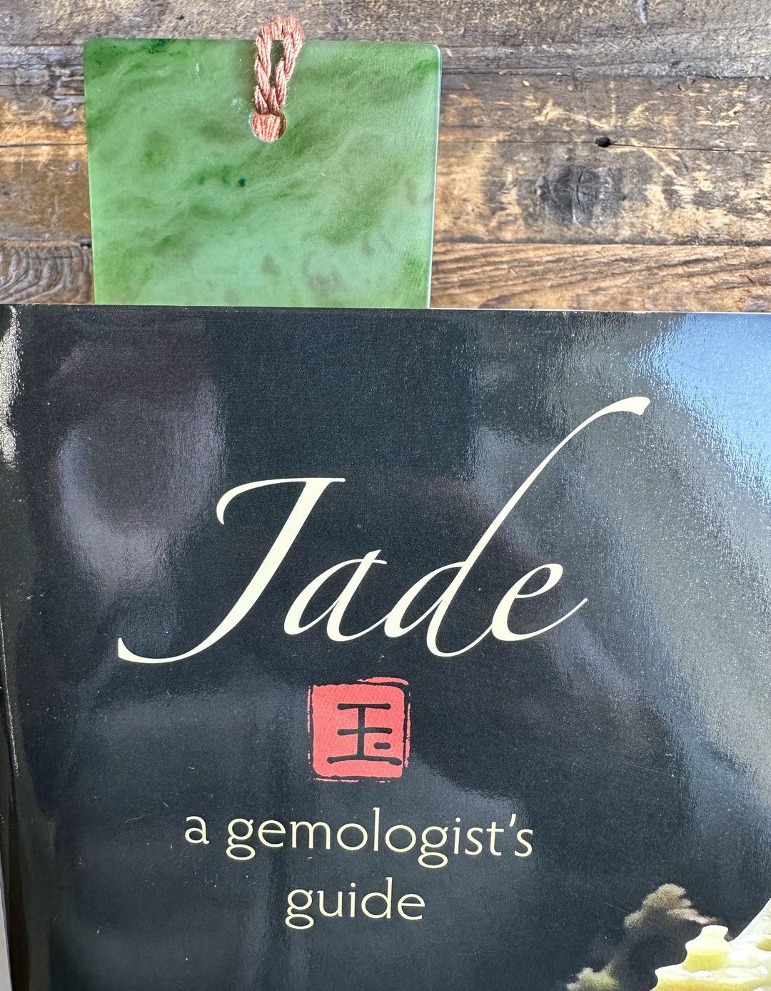 Green jade bookmark resting on a glossy black book cover that reads Jade a gemologist&