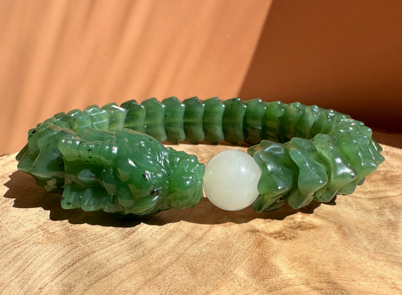 A carved green jade bracelet with a textured, segmented design and a smooth white central bead, displayed on a wooden surface.