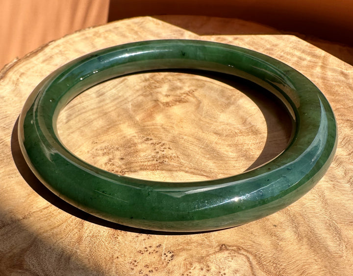 A round green jade bangle bracelet displayed on a natural wood slice background.