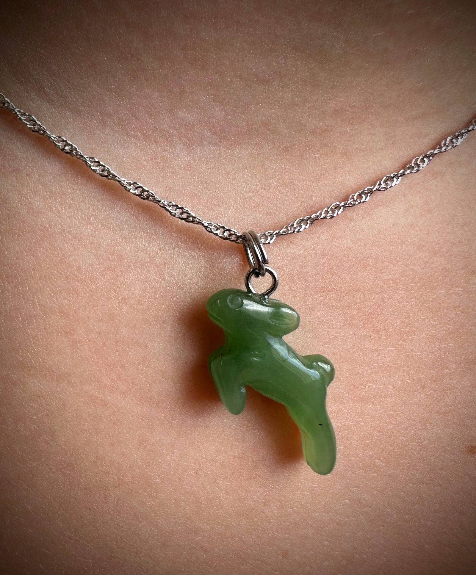 A close-up of a silver chain necklace with a polished green jade pendant shaped like a small animal, worn on a person's neck.