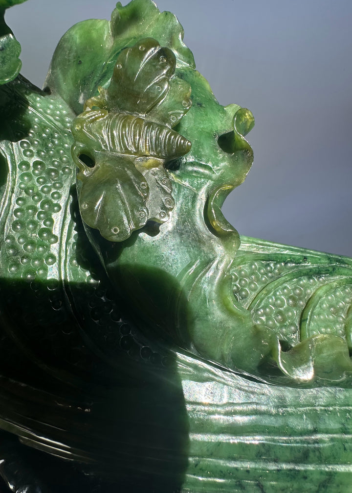 Side view of the hand carved jade Chinese cabbage with detailed leaves resting on a wooden stand.