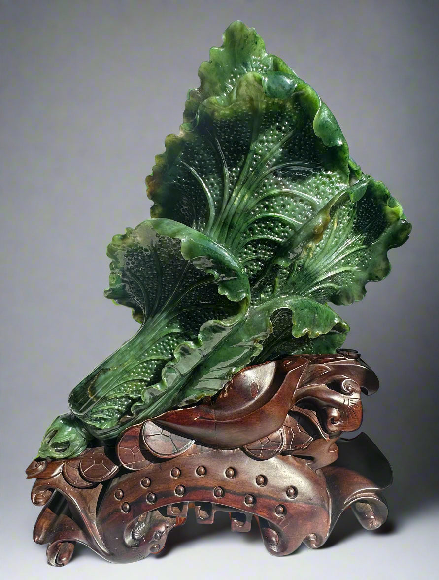 Close up of green jade cabbage leaves with detailed veining on a carved wooden base.