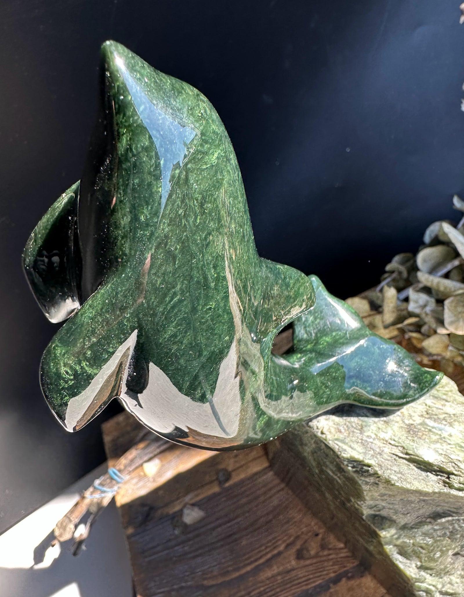 Dark green Canadian jade dolphin sculpture perched on a jagged jade base against a dark background