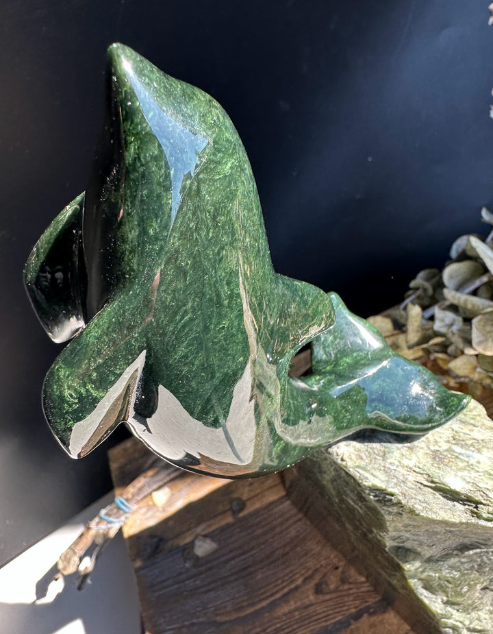 Dark green Canadian jade dolphin sculpture perched on a jagged jade base against a dark background