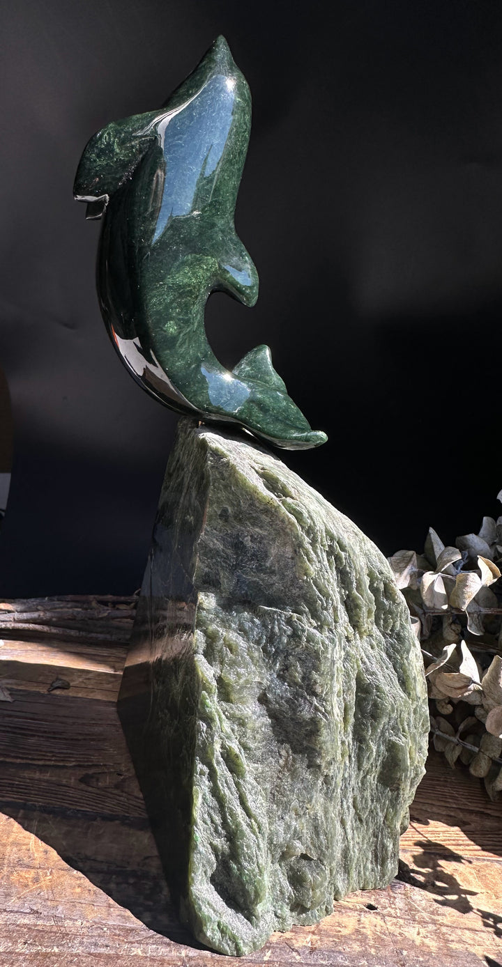 Dark green Canadian jade dolphin sculpture perched on a rough jade base.