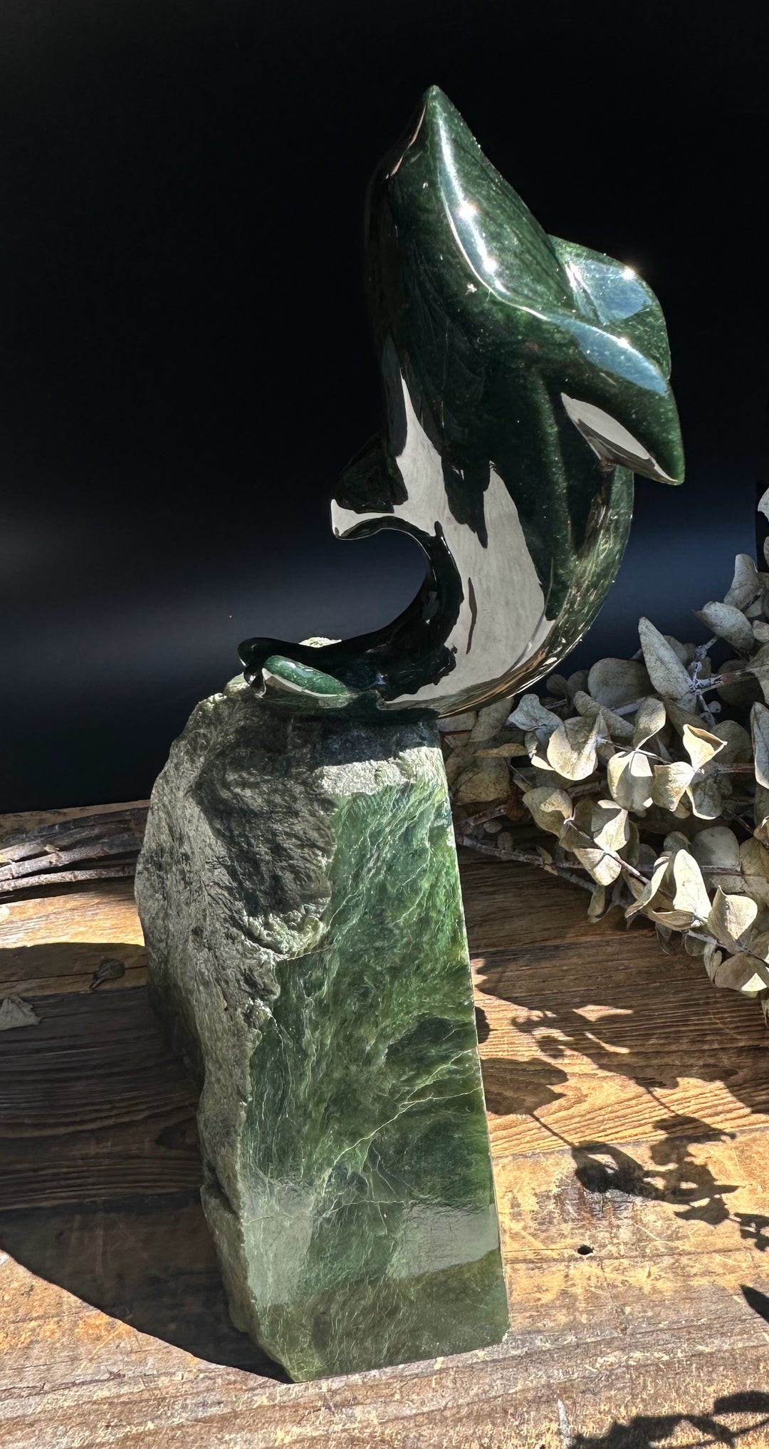 Dark green jade dolphin statue atop a tall rugged jade pedestal with a glossy finish