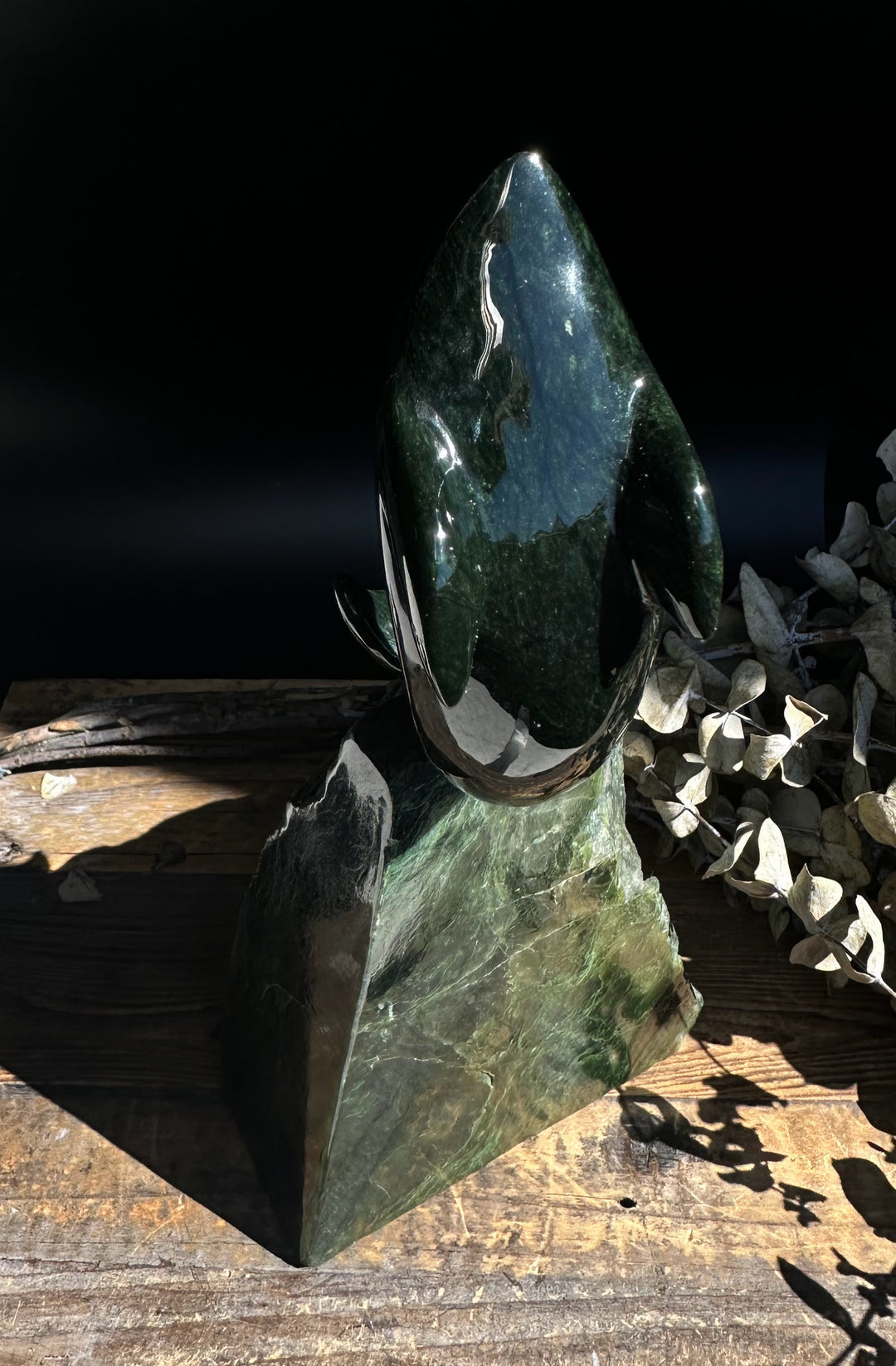 Dark green jade dolphin on an angular tall jade base shown in bright sunlight