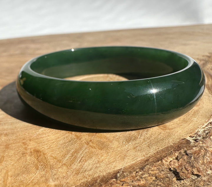 Green nephrite jade bangle with a smooth glossy finish resting on a wooden surface.