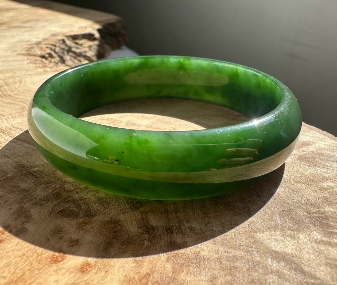 Vivid green nephrite jade bangle with lighter inner banding on a wooden surface