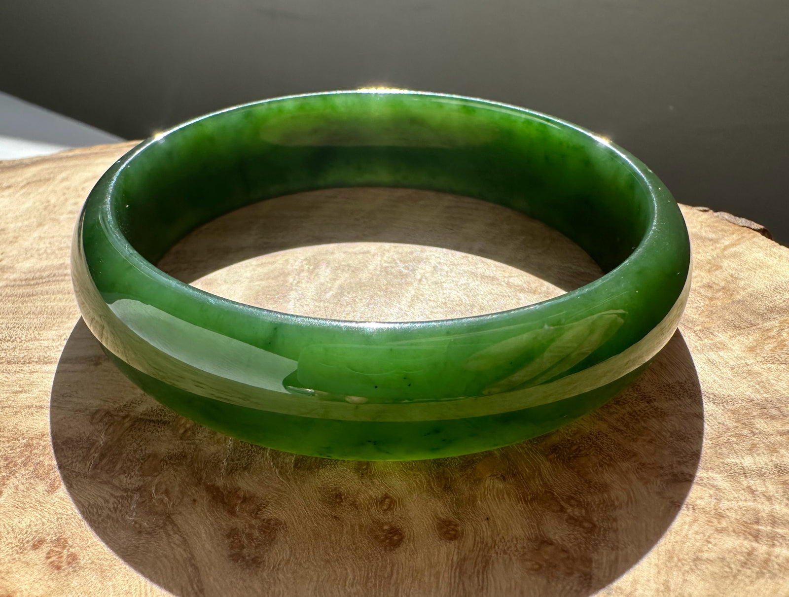 Canadian nephrite jade bangle 54 x 13.5 mm in bright green resting on a wooden surface