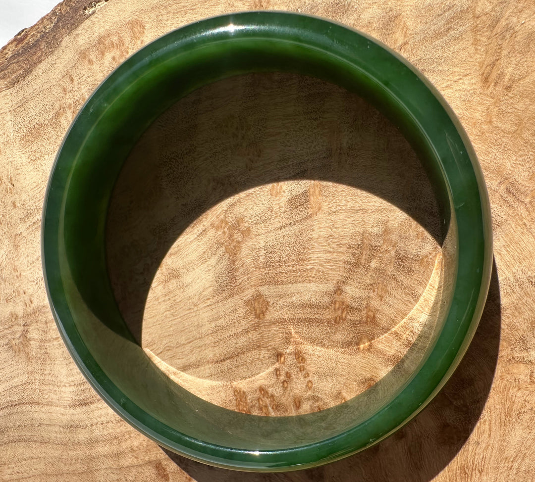 Canadian nephrite jade bangle in deep green viewed from above on a wooden surface